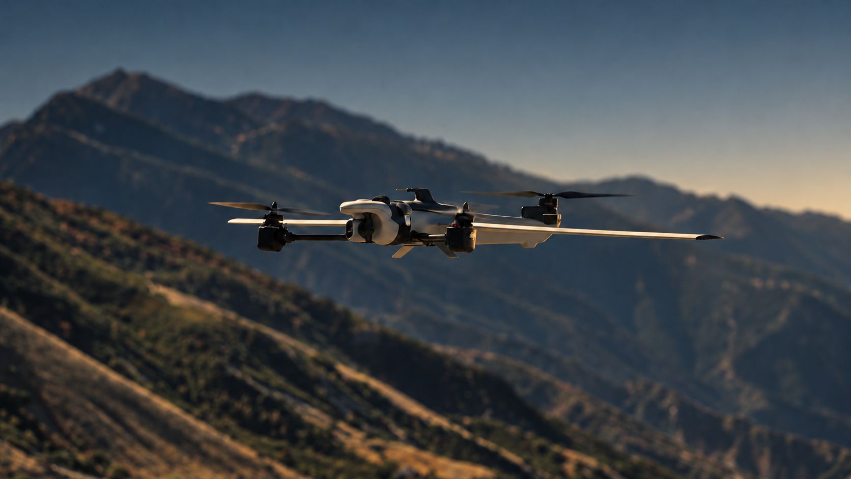 Fixed-wing VTOL aircraft cruising above a mountain ridge at dusk